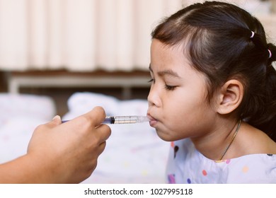 Mother Giving Medicine To Her Daughter. Sick Asian Little Child Girl Getting Liquid Medicine With Syringe In The Hospital.