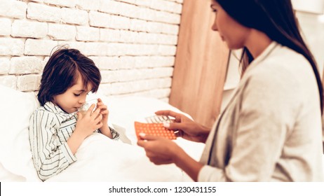 Mother Giving Medicine To Sick Son Lying Bed. Caring Mom Giving Sick Boy Pills. Worried Mother Giving Glass Of Water To Ill Kid. Hospital Concept. Healthy Concept. Parent Concept.