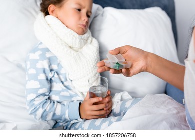 mother giving pills to sad, diseased daughter holding glass of water on blurred background - Shutterstock ID 1857206758