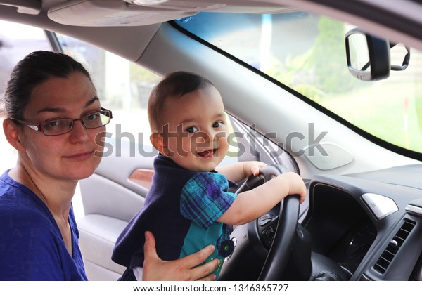 Mother in\
glasses teaching her baby to drive a\
car