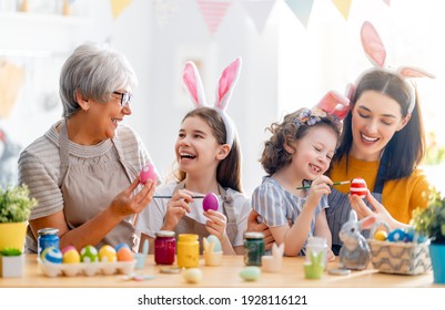 Mother, Grandma And Children Are Painting Eggs. Happy Family Are Preparing For Easter. Cute Little Girls Wearing Bunny Ears.