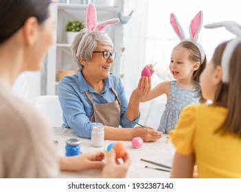 Mother, Grandma And Children Are Painting Eggs. Happy Family Are Preparing For Easter. Cute Little Girls Wearing Bunny Ears.