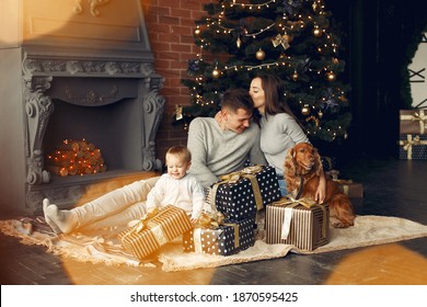 Mother In A Gray Sweater. Family With Christmas Gifts. People Near Fireplace. Family With Dog.