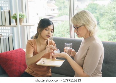 Mother And Grow Daughter Share Time Together At Home. Senior Woman Taking Pills Medicine.  Granddaughter Take Care Older With Love. Concept Family Mix Skin Of Stepmother, Daughter-in-law And Adoption