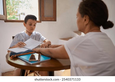 A mother guides her son through a homeschooling session at a wooden table, fostering learning in a sunlit room. - Powered by Shutterstock