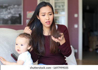 Mother hair loss postpartum.Young asian mommy having problem with hair because the hormonal changes after birth she sitting on sofa with her baby at home.