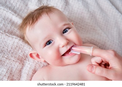 Mother Hands Brushing Teeth With A Finger Brush Of A Happy Infant Baby. Mom Doing Oral Hygiene To A Smiling Toddler Kid, Six To Seven Months Old