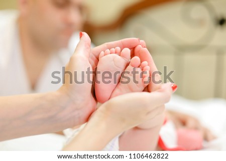 Mother hands holding little legs of newborn baby, father in background. Concept of babes and family.