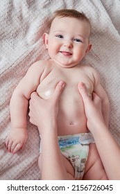 Mother Hands Are Smearing Cream On A Happy Infant Baby. Mom Massages A Smiling Toddler Kid On A Sofa, Six To Seven Months Old