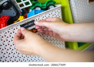 Mother Hands Sticking Printing Label Sticker With Name Title Of Toy For Comfortable Storage And Sorting In Plastic Case Box. Woman Arms Use Marker Method For Space Organizing At Children's Room