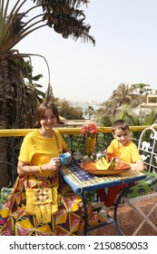 Mother Has Breakfast With Her Son On Ngor Island, Senegal, Africa. Table Layout, Table Setting For Breakfast. Woman With Child, Kid And Food. Tourist People Has Breakfast In Senegal, Africa. Banana