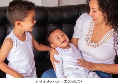 Mother having a beautiful time with her two children. Smiling brothers sitting on a sofa next to their mother. Concept of happy family. Two latin children.