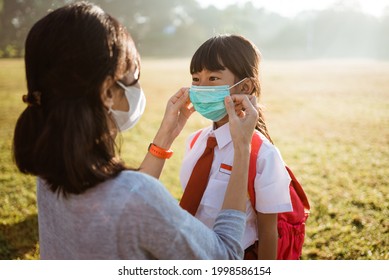 mother help her daughter to put on the mask before going to school in the morning