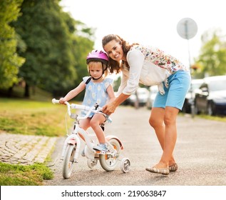 Mother Helping Baby Girl Riding Bicycle