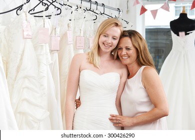 Mother Helping Daughter To Choose Dress In Bridal Store