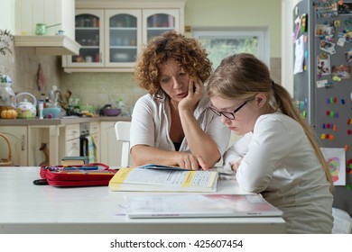Mother helping daughter with her homework at the table in the dining room. Home Schooling concept.