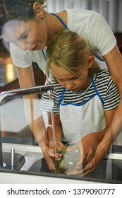 Mother Helping Daughter To Watch Glass In Kitchen Sin