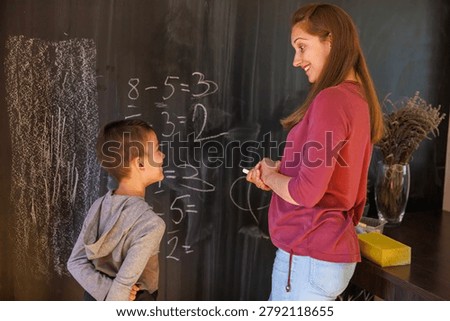 Mother helping first grade elementary school son study math for school, practicing on chalkboard