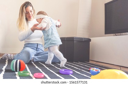 Mother Helping Her Daughter At First Steps In Home - Baby Girl Walking And Holding Hands With Her Mum - Family Concept