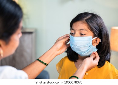 Mother Helping Her Daughter To Wear Face Mask Before Going To School At Home As Coronavirus Covid-19 Healthcare Safety Measures - Concept Of Back To School