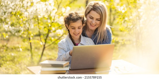 Mother Helping Her Little Daughter To Use Laptop Computer. Child Studying At Home Doing Her Homework Or Having Online Lesson. Homeschooling Concept.