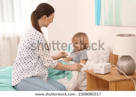 Mother helping her sick son with nebulizer inhalation in bedroom