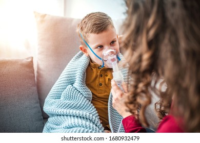 Mother helping little son using nebulizer during inhalation. Mother helps her little boy to makes inhalation at home. Little boy having inhalation for easing cough