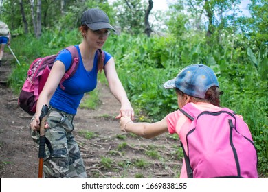 Mother helps her daughter climb a mountain.  Travelers teamwork. tourists with backpacks help climb each other up hill. Concept of mother's care of her child. Family of tourists travelling with kids.