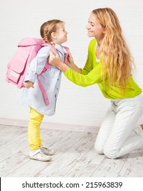 Mother Helps Her Daughter Get Ready For School. Mom Support Child To Wear A Backpack