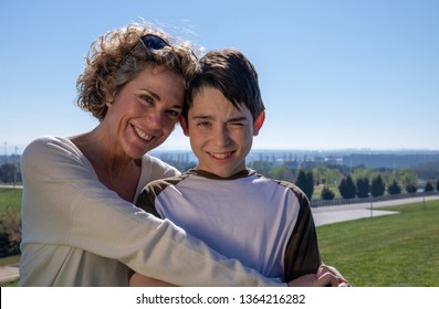 Mother With Her 12 Year Old Son In A Loving Attitude On A Summer Day In A Public Park.