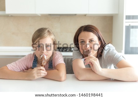 Mother with her 12 years old daughter sitting in the kitchen eating ice cream. Good relations of parent and child. Happy moments together