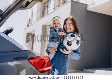 Mother with her baby daughter by the car with football ball