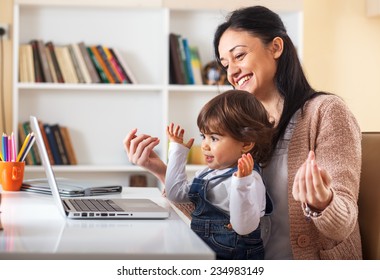 Mother and her baby girl listening to music on laptop.They sitting in living room.Natural light ambient. - Powered by Shutterstock