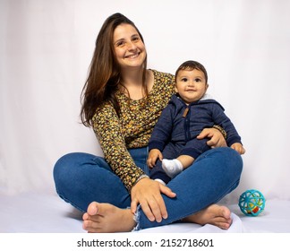 Mother And Her Baby Son Smiling On A White Background. Mention The Iteration Between Mother And Child, Parental Care That Provides Children With Joy In Their Daily Lives.