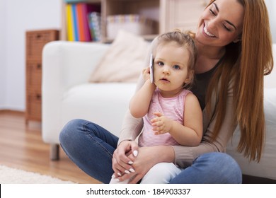 Mother And Her Baby Using Mobile Phone At Home 