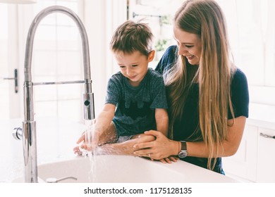 Mother With Her Child Playing With Water In Kitchen Sink At Home. Happy Lifestyle Family Moments.