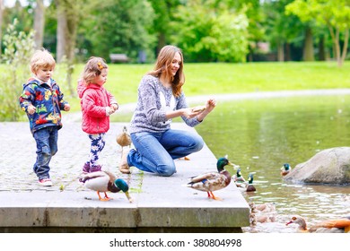 Mother And Her Children Feeding Ducks In Summer Park, Adorable Kid Boy And Girl, Siblings Having Fun Together