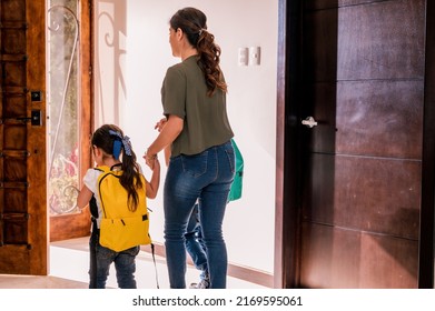 Mother And Her Children Leaving The House On Their Way To School. Elementary School Children In Uniform And Backpack.