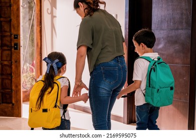 Mother And Her Children Leaving The House On Their Way To School. Elementary School Children In Uniform And Backpack.