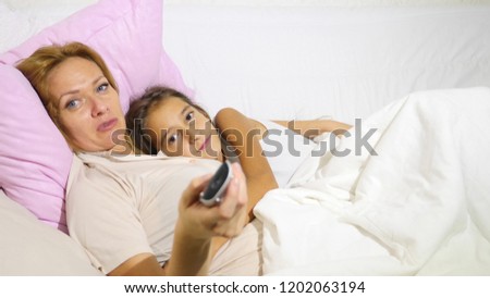 the mother and her children lying in bed, they watch TV together and switch the channels to the control panel. Copy space