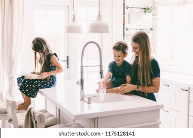 Mother with her children playing with water in kitchen sink at home. Happy lifestyle family moments.