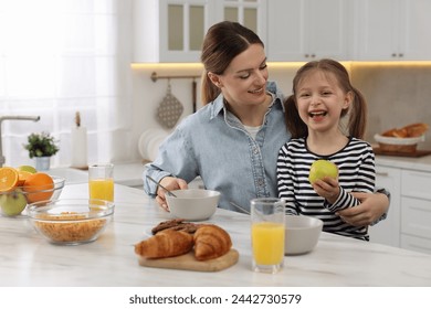 Mother and her cute little daughter having breakfast at table in kitchen - Powered by Shutterstock