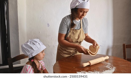 A mother and her daughter in chef hats and aprons baking together at a wooden table. The scene captures family bonding, teaching, and homemade experiences. - Powered by Shutterstock