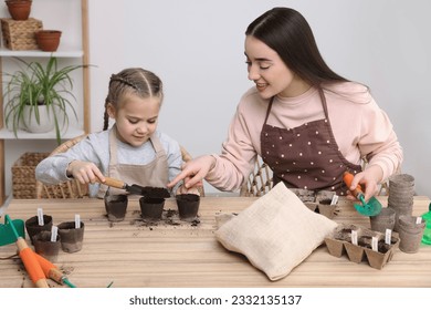 Mother and her daughter filling pots with soil at wooden table indoors. Growing vegetable seeds - Powered by Shutterstock