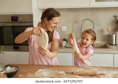 Mother and her daughter kneading dough at wooden table in kitchen - Powered by Shutterstock