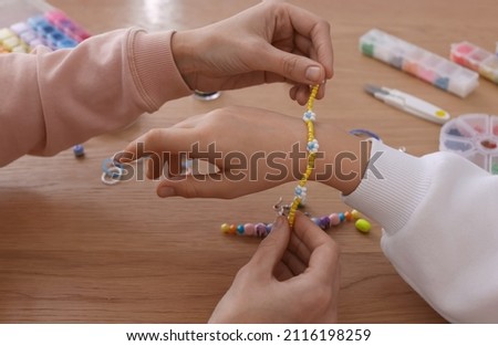 Mother with her daughter making beaded jewelry at table, closeup