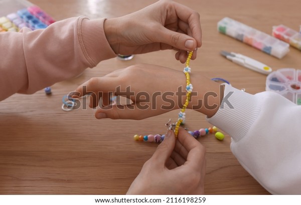 Mother with her daughter making beaded jewelry at\
table, closeup