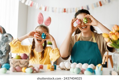 Mother and her daughter painting eggs. Happy family preparing for Easter. Cute little child girl wearing bunny ears. - Powered by Shutterstock