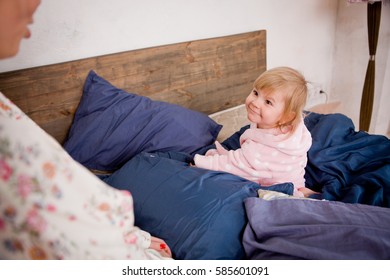 Mother With Her Daughter In A Pillow Fight On The Bed. They Are Happy And Having Fun. Play In The Morning Together. The Sleeping Girl's Clothes Having Fun. In Her Hair And In Robes At Home