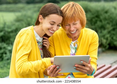 Mother with her daughter using digital tablet dressed in yellow in the park - Powered by Shutterstock